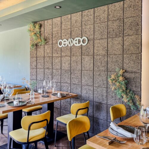 Zona del comedor con el logotipo de Canedo en la pared y sillas amarillas